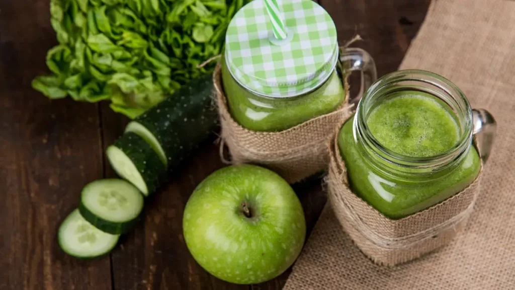 Dos termo termos de jugos verde rodeado de una manzana verde, un pepino y lechuga