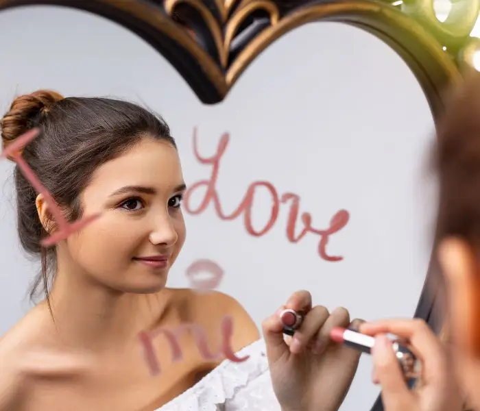 Mujer frente al espejo escribiendo 'I love me' en el vidrio, representando la importancia del amor propio y la autoaceptación.